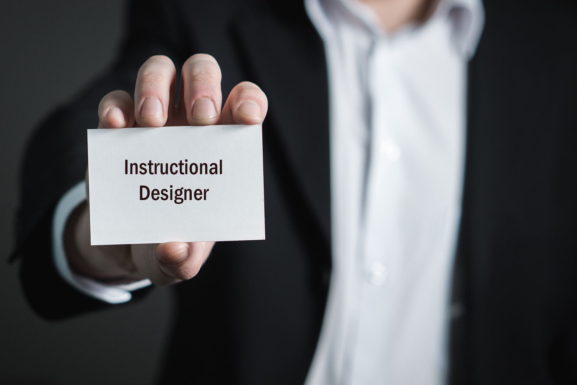 This is an image of a professional holding up a business card with the title of "Instructional Designer."